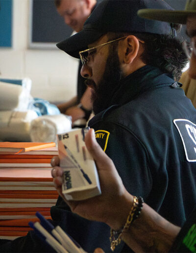 Two officers distribute pens and notebooks to individuals in custody.