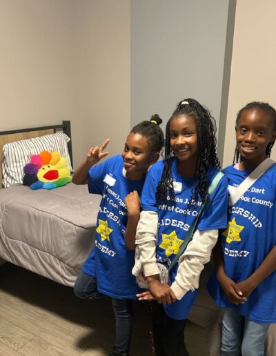 Three children pose for a camera in front of a bed