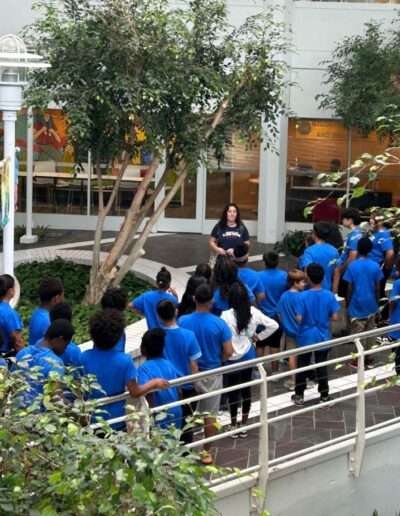 A woman addresses a group of children in the middle of a courtyard